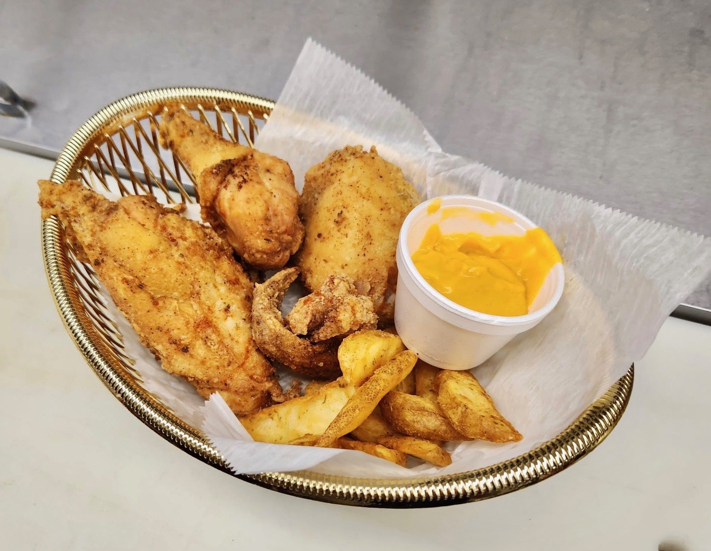 Basket of golden fried chicken with seasoned potato wedges and a side of cheese sauce from The Chicken Shack in Waupaca, WI