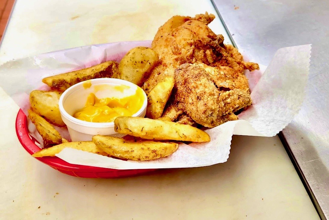 Red basket of fried chicken with seasoned potato wedges and cheese sauce from The Chicken Shack in Waupaca, WI